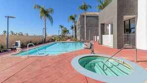 A swimming pool with a red tiled deck, a hot tub, and palm trees in the background. - Studio 6 Suites Perris, CA (Perris)