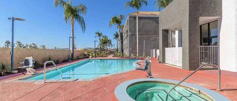 Ein Swimmingpool mit roter Fliesenverkleidung, einer Whirlwanne und Palmen im Hintergrund.