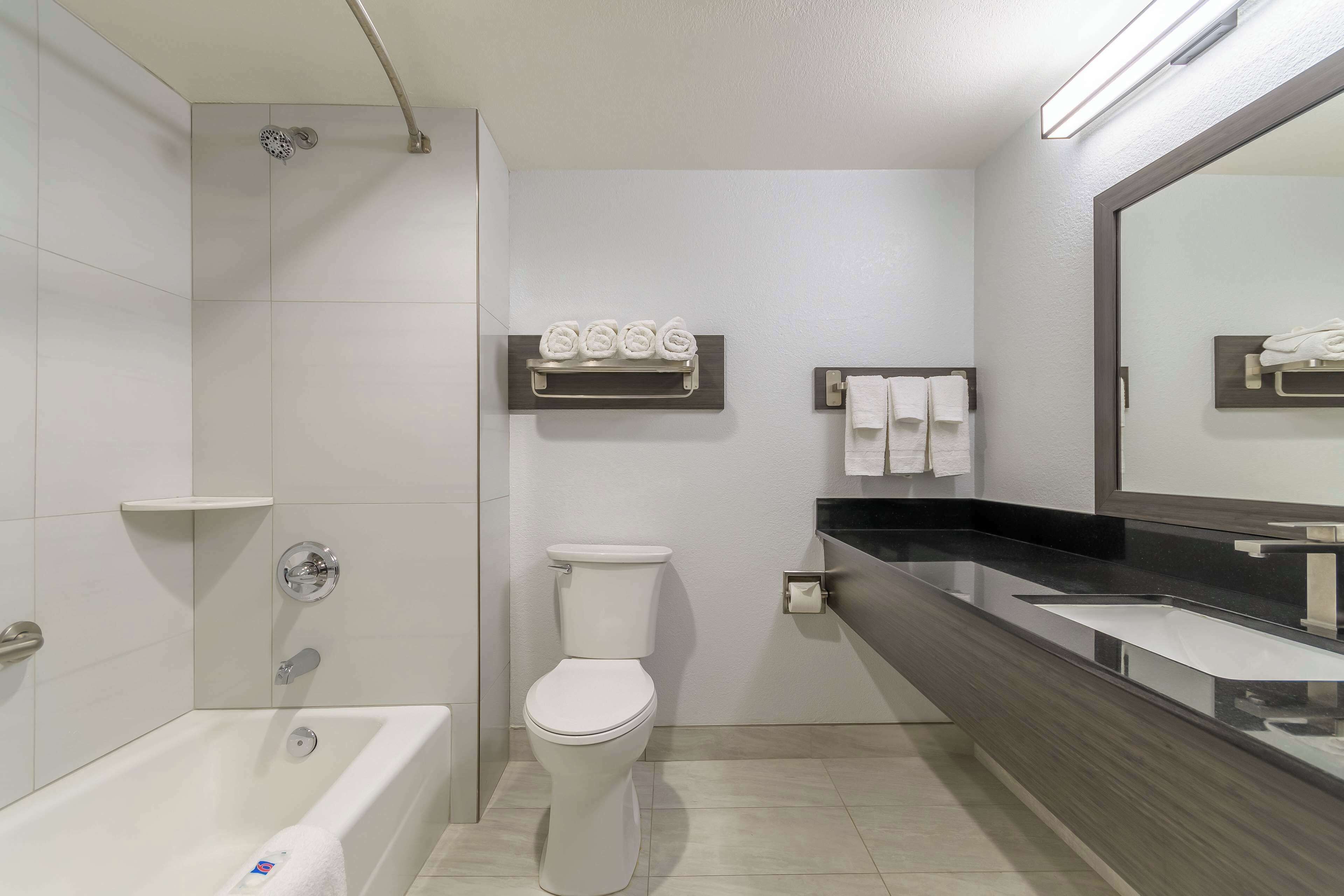 A modern bathroom with a bathtub, toilet, and a large mirror.