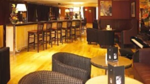 A bar area with multiple seating options including bar stools and chairs, a piano, and a counter with a lamp. - Pery's Hotel (Limerick)