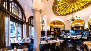 A spacious dining area with high ceilings, large windows, and a central chandelier. Tables are set with white tablecloths and wine glasses. - Astra Hotel Vevey (Vevey)
