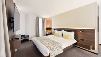 A modern hotel room with a large bed, bedside tables, a flat-screen TV, and a built-in nightstand.