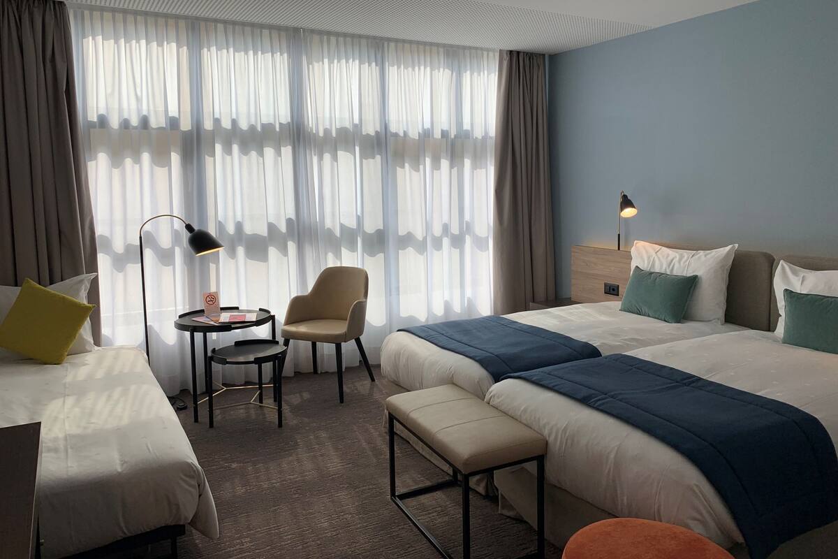 Ein Hotelzimmer mit zwei Betten, einem Schreibtisch mit Stuhl, einem kleinen Tisch und einer Lampe.
