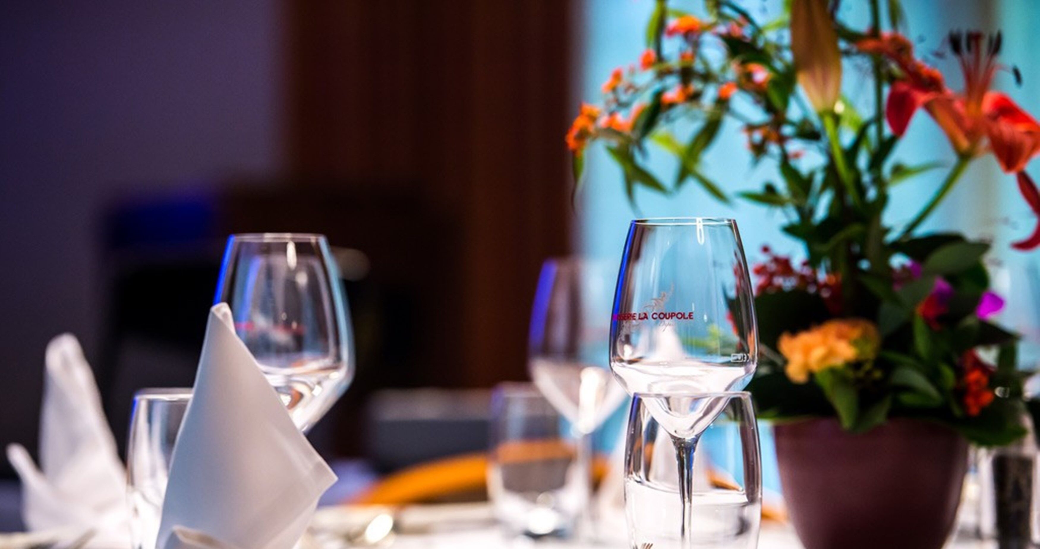 Una mesa de comedor con copas de vino y una maceta con flores.