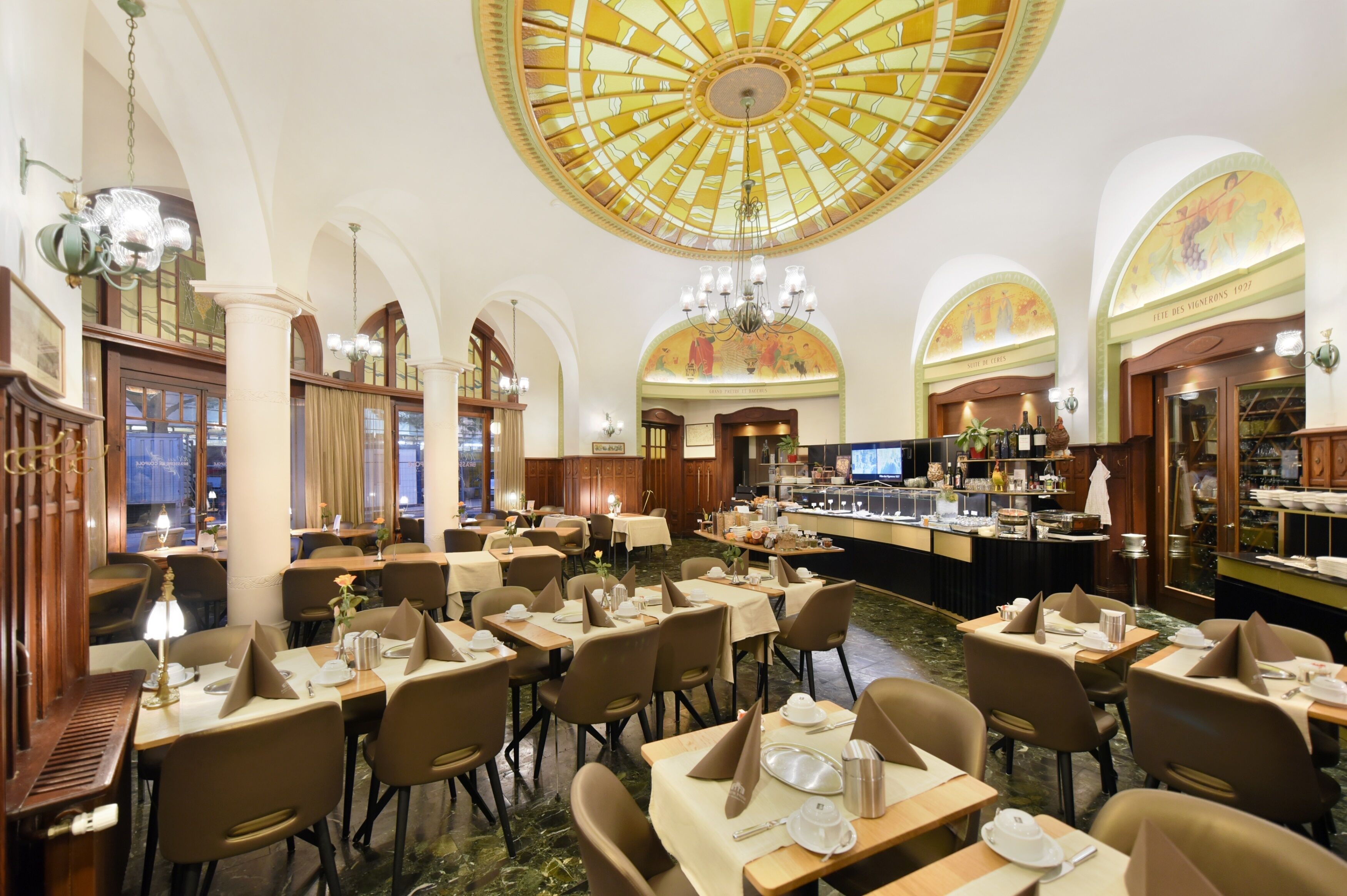 A spacious dining area with multiple tables and chairs, a central bar, and a large, ornate ceiling.