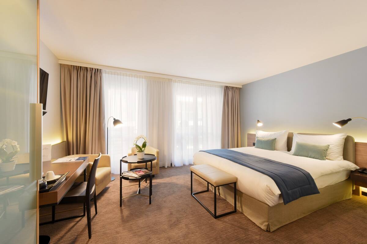 Ein Hotelzimmer mit Bett, Schreibtisch, Stuhl, einem kleinen Tisch und einer Zimmerpflanze.