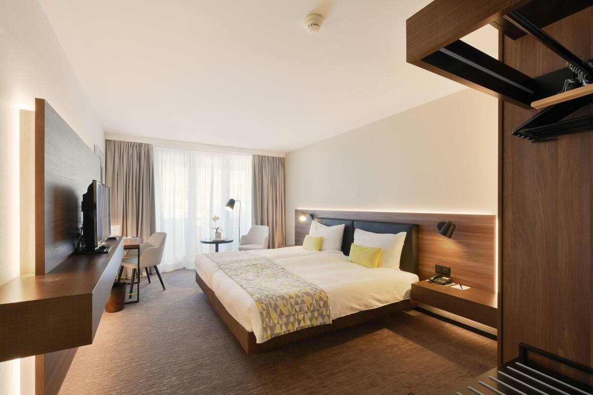 Ein modernes Hotelzimmer mit einem großen Bett, einem Schreibtisch, einem Stuhl und einem kleinen Tisch.