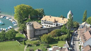 A castle with a moat, surrounded by greenery and a body of water. - Astra Hotel Vevey (Vevey)