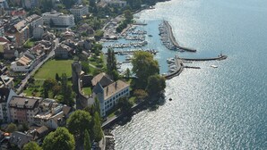 An aerial view of a coastal town with a marina, buildings, and a castle-like structure. - Astra Hotel Vevey (Vevey)
