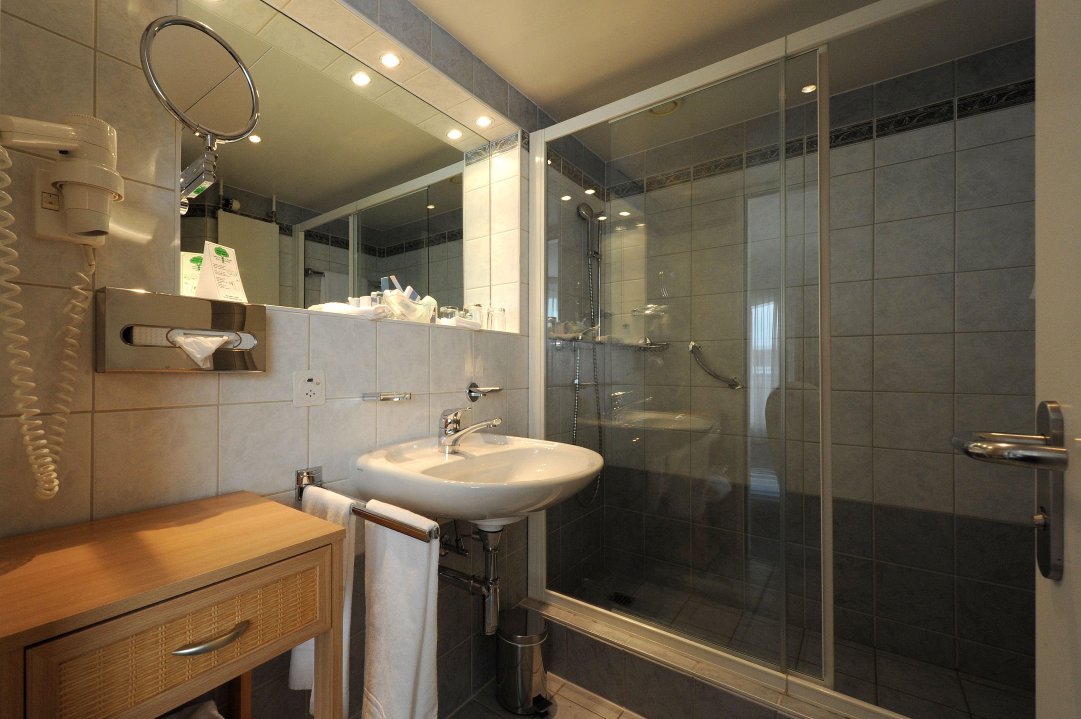 A modern bathroom with a glass-enclosed shower, a white sink, and a wooden vanity.