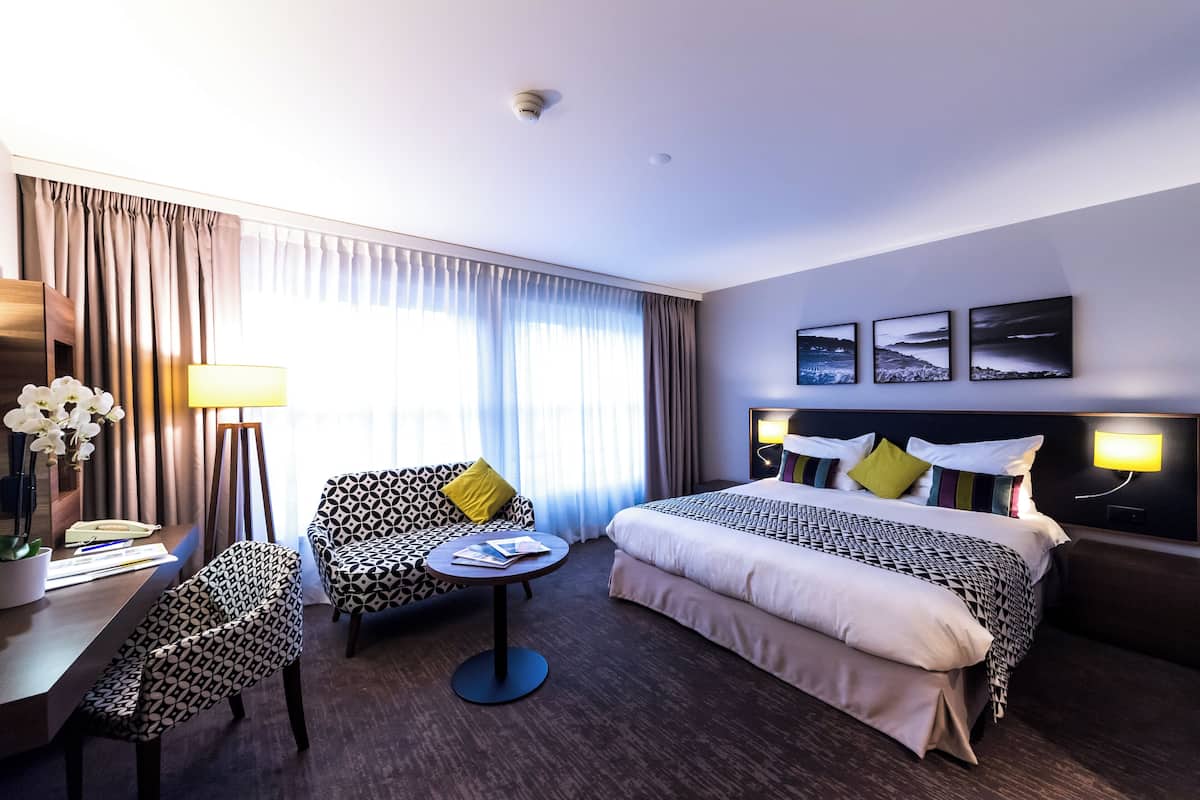 Ein Hotelzimmer mit Bett, Schreibtisch mit Lampe, Stuhl und einem kleinen Tisch.