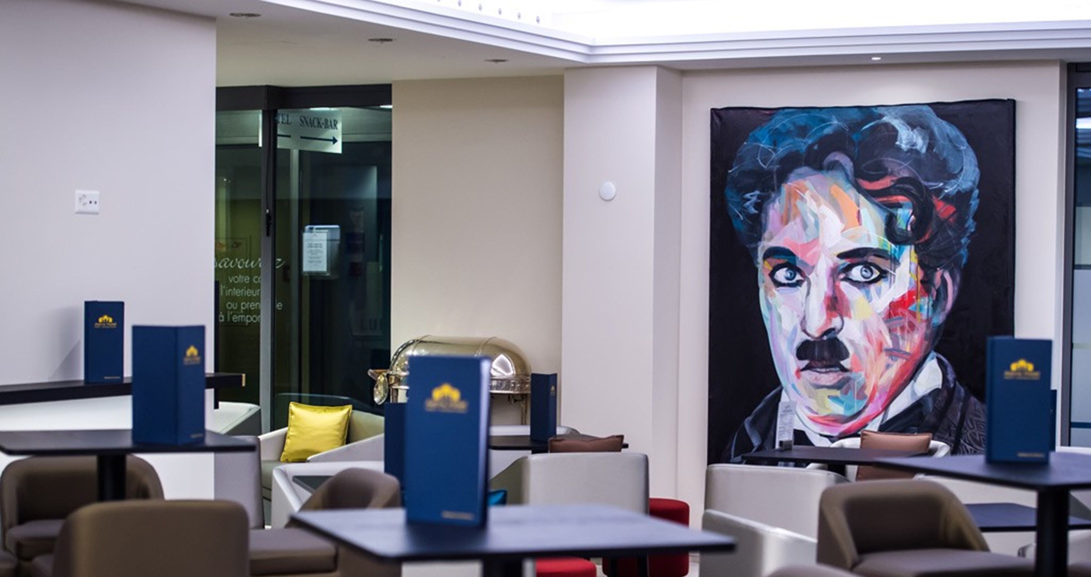 Un hall d’hôtel moderne, agrémenté d’un grand tableau abstrait, de coins salon et d’un bar à collations bien visible.