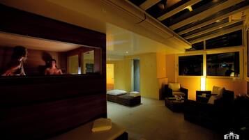 A modern hotel room with a large window, a sofa, a small table, and a massage table.