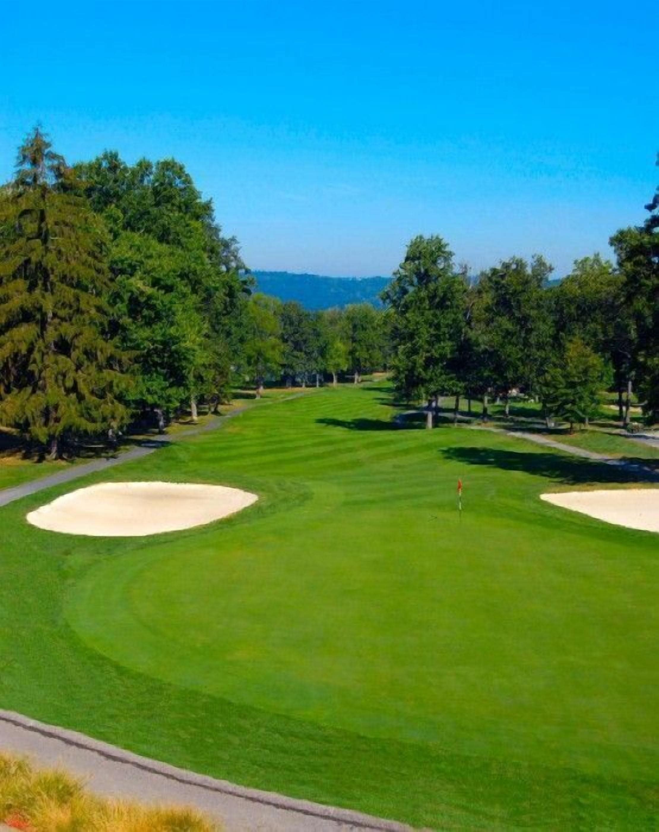 Ein Golfplatz mit gepflegten Spielbahnen, Sandbunkern und blauem Himmel.