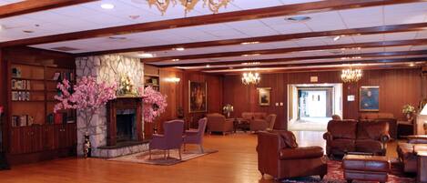 A spacious lobby with wooden floors, a stone fireplace, and a large chandelier. There are several leather sofas and armchairs arranged for seating.