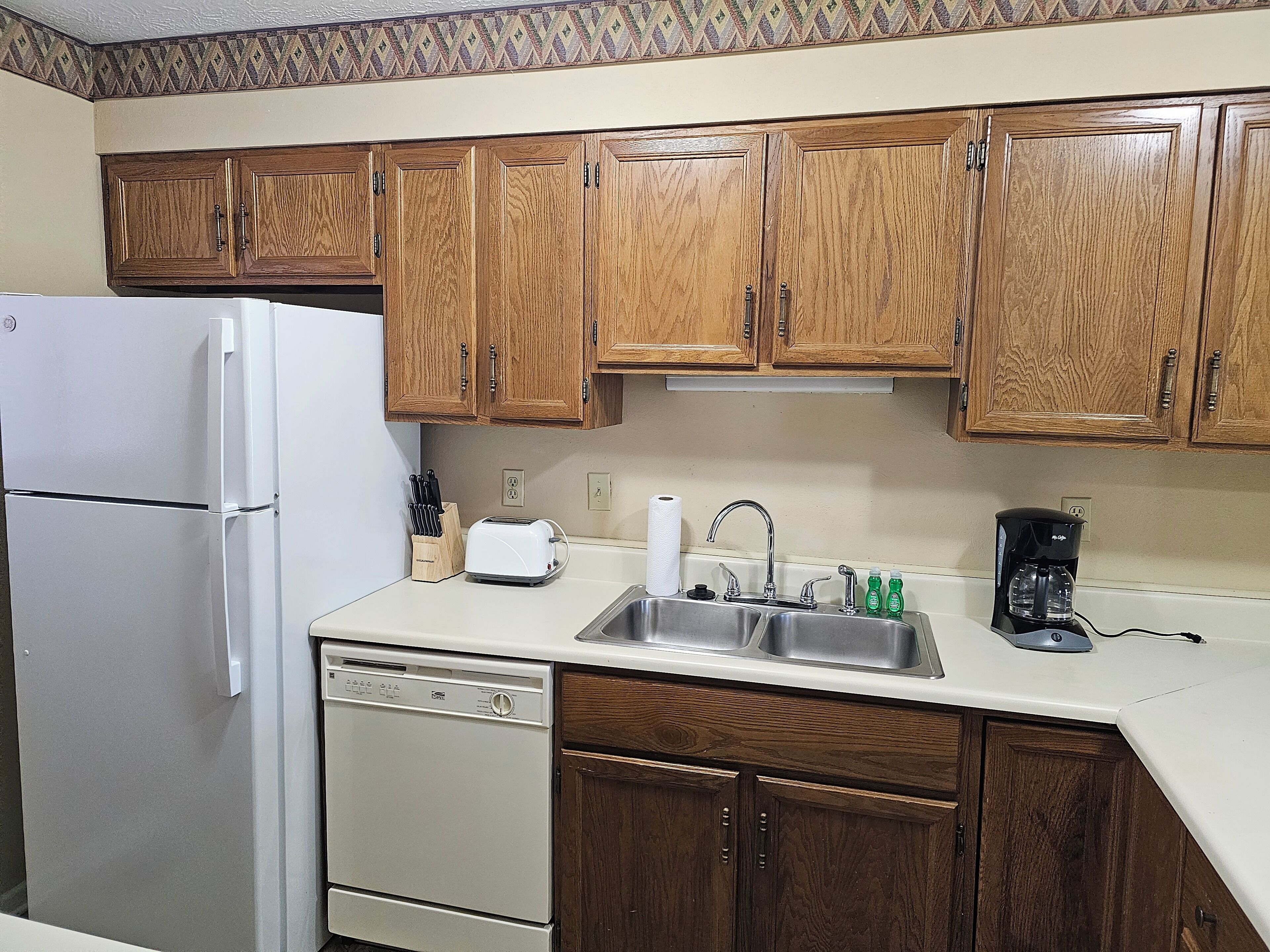 A kitchen with wooden cabinets, a white refrigerator, a dishwasher, a sink with a faucet, and a coffee maker.