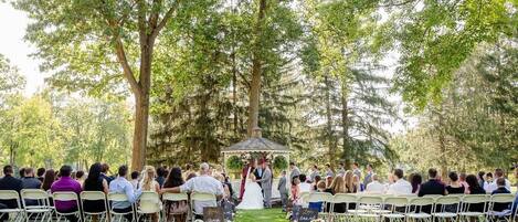 A wedding ceremony outdoors with guests seated on chairs facing a gazebo.