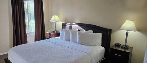 Una cama bien tendida con sábanas blancas, dos mesitas de noche con lámparas y una ventana con cortinas.