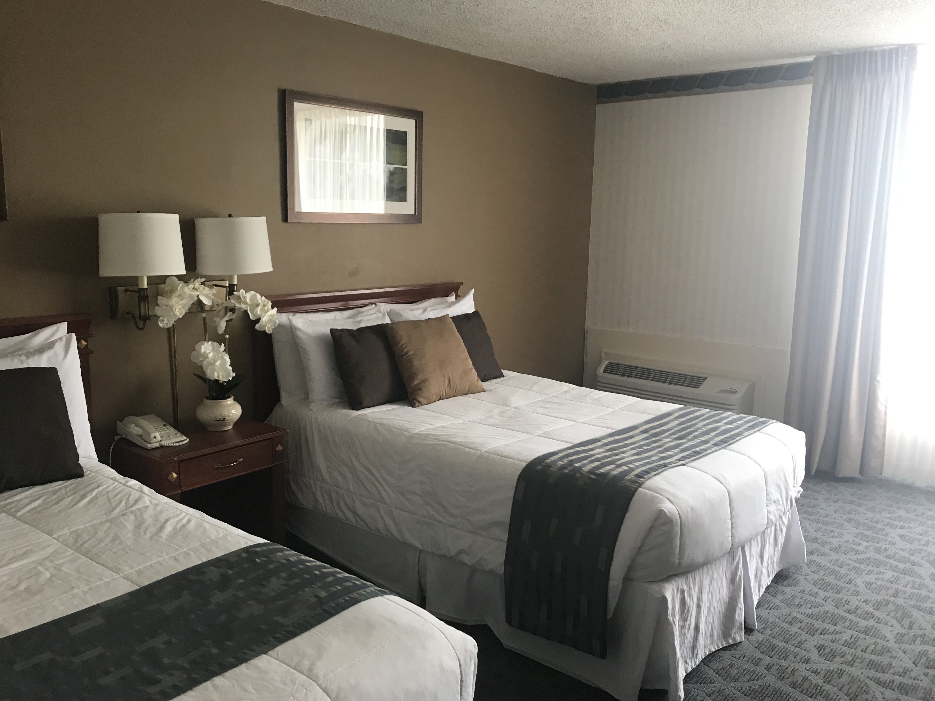 Habitación de hotel con dos camas, una mesita de noche con teléfono, lámparas y un jarrón con flores.