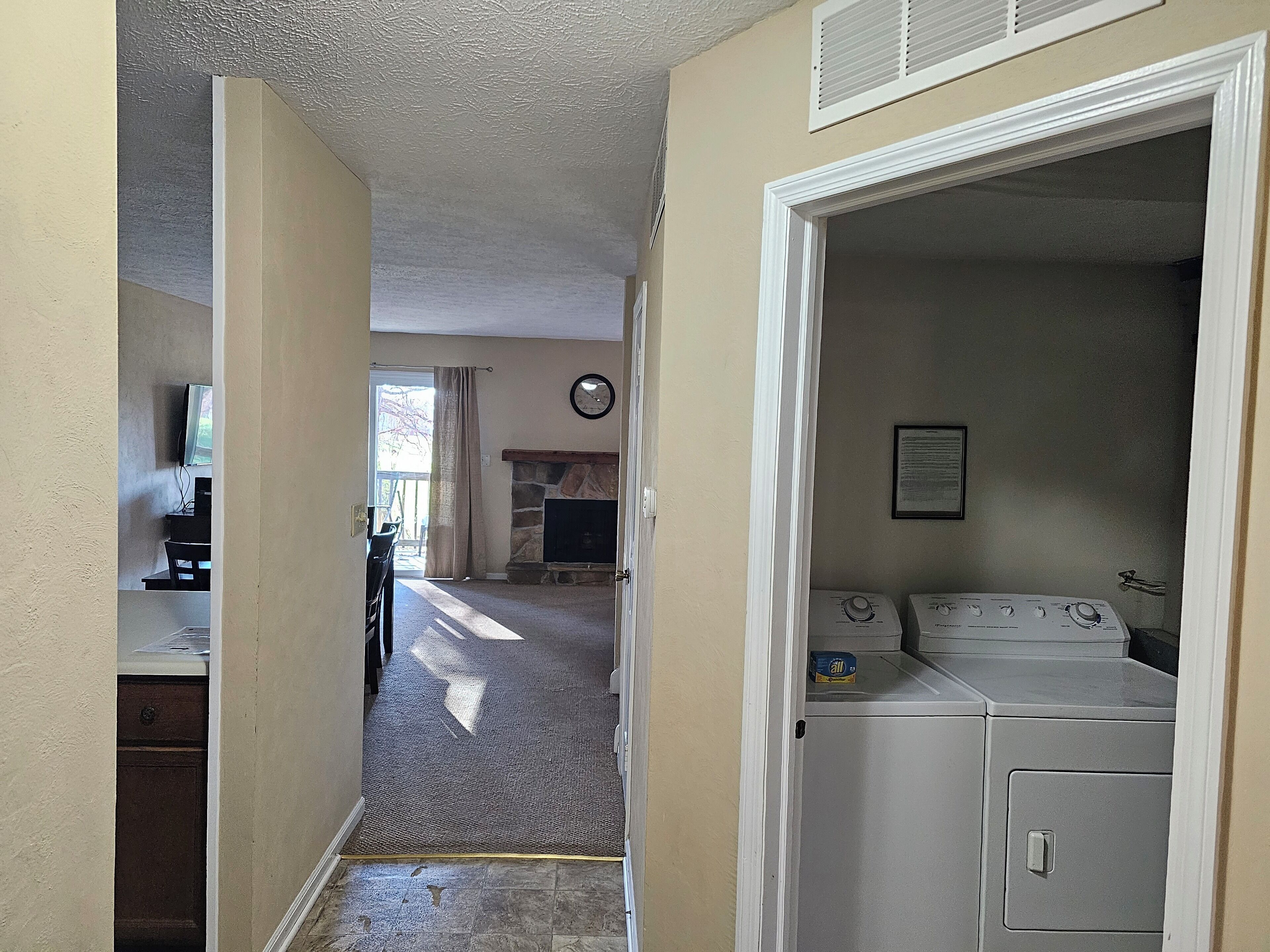 A laundry room with a washer and dryer, a stone fireplace, and a television in the background.