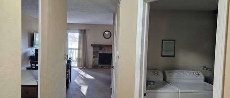 A laundry room with a washer and dryer, a stone fireplace, and a television in the background.