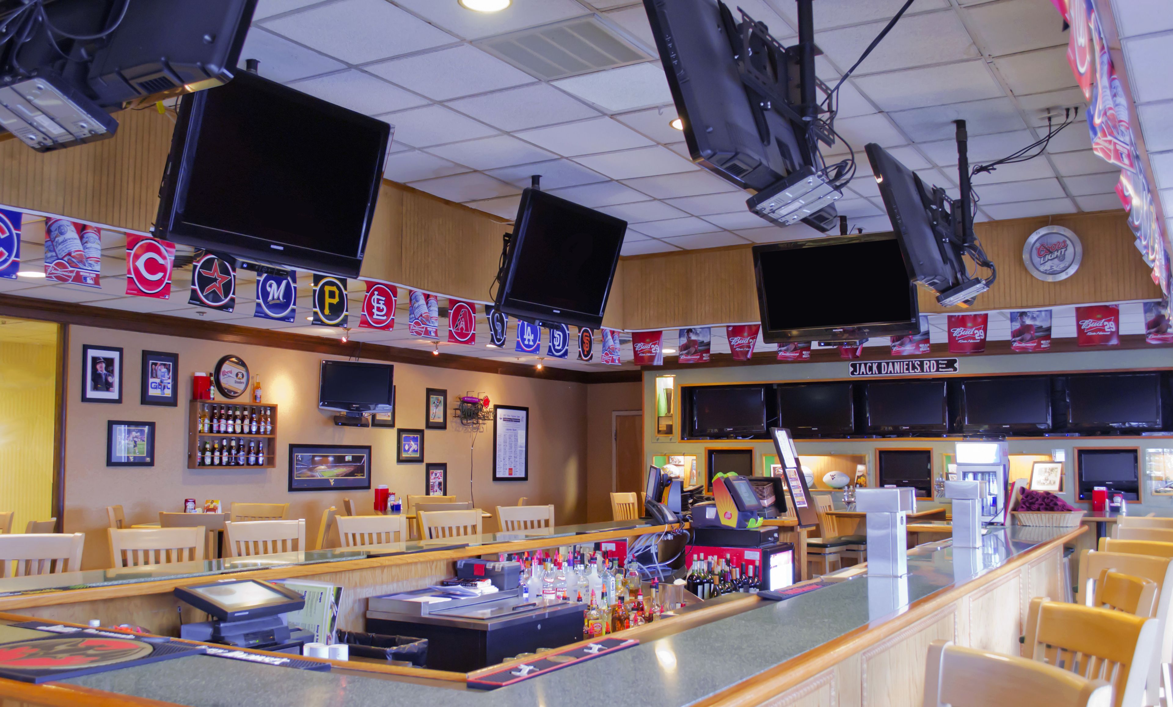 Een bar met meerdere televisies, een toonbank met diverse flessen, en een bord met de tekst 'Jack Daniel's Road'.
