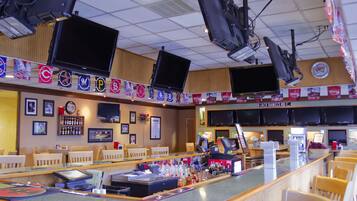 Een bar met meerdere televisies, een toonbank met diverse flessen, en een bord met de tekst 'Jack Daniel's Road'.