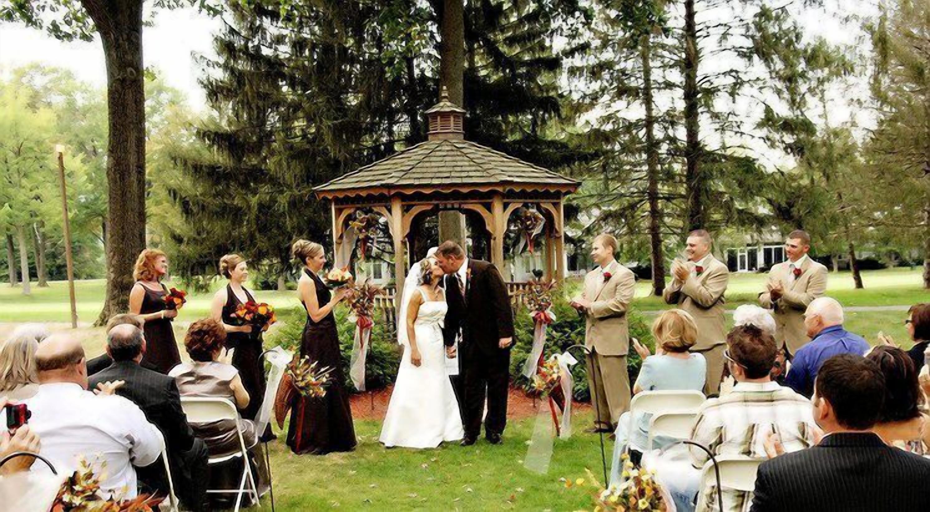 Un espacio para bodas tipo pérgola, con invitados sentados en sillas frente al pasillo.