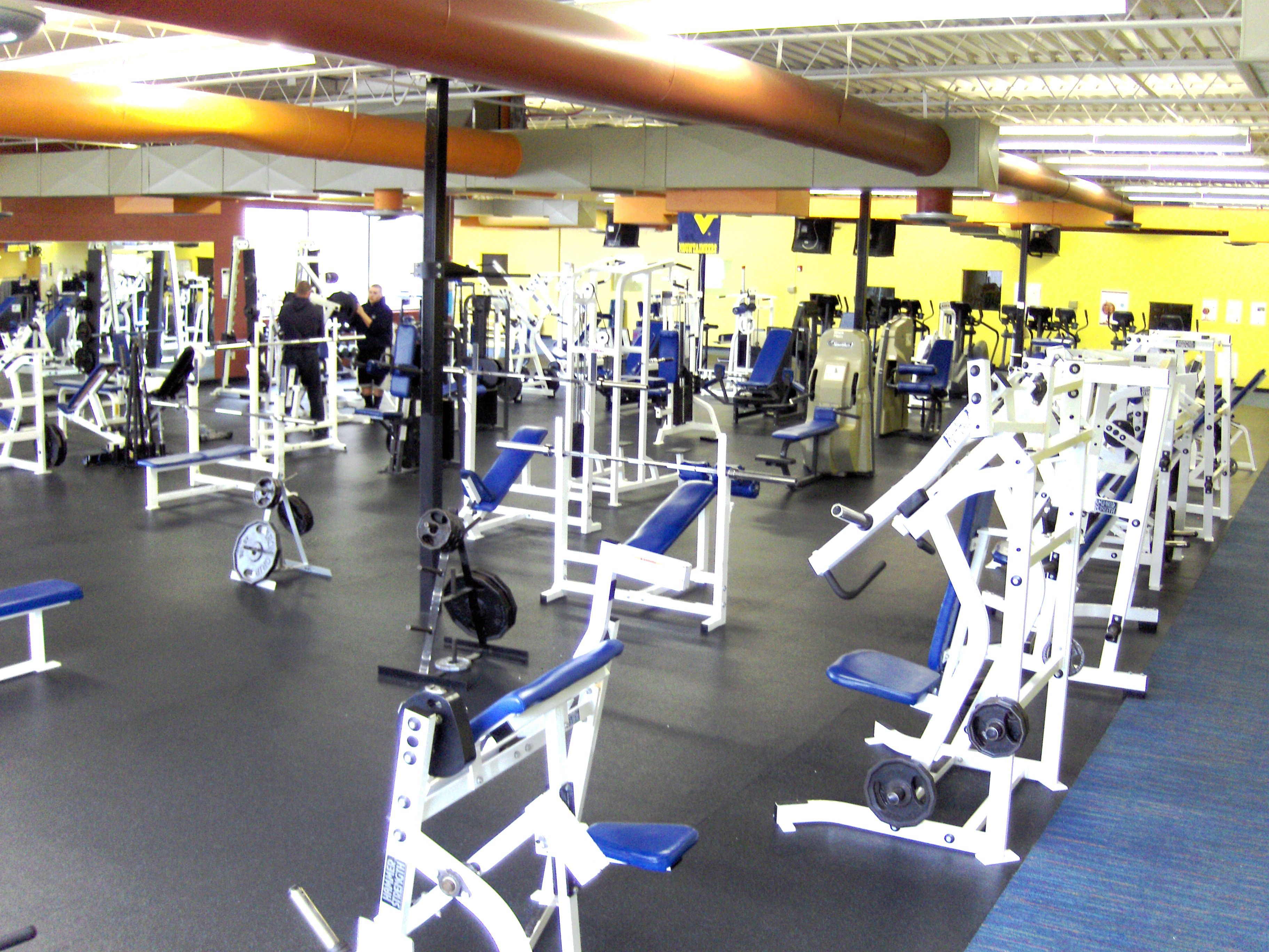 Une salle de sport équipée de divers appareils d’exercice, notamment des machines de musculation et des bancs.