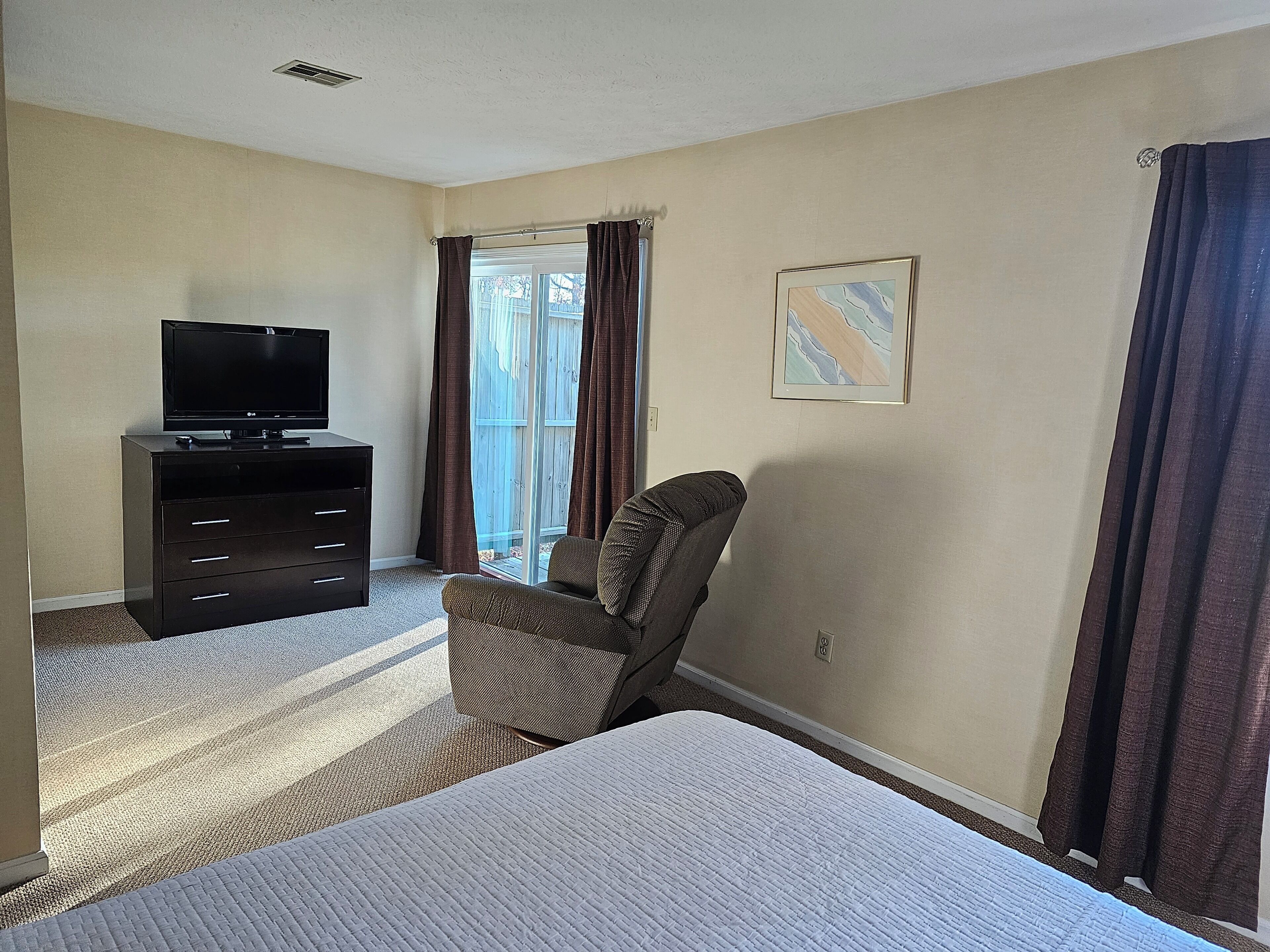 A hotel room with a bed, a TV on a dresser, a chair, and a window with curtains.