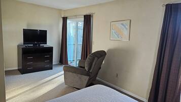 A hotel room with a bed, a TV on a dresser, a chair, and a window with curtains.