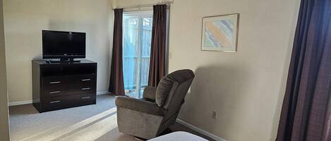 Ein Hotelzimmer mit einem Bett, einem Fernseher auf einer Kommode, einem Sessel und einem Fenster mit Vorhängen.