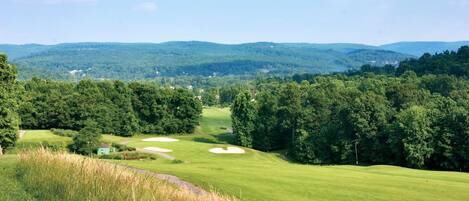 A golf course with rolling hills and dense forests in the background.
