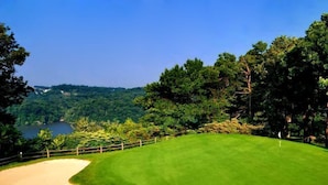 A golf course with a sand bunker, a flagstick, and a view of a lake surrounded by trees. - Lakeview Golf Resort (Morgantown)