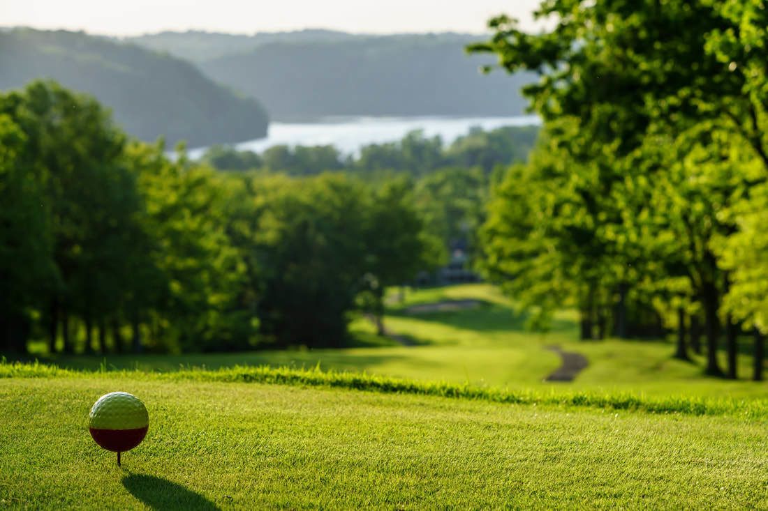 A golf ball on a well-maintained green with a lake and trees in the background.