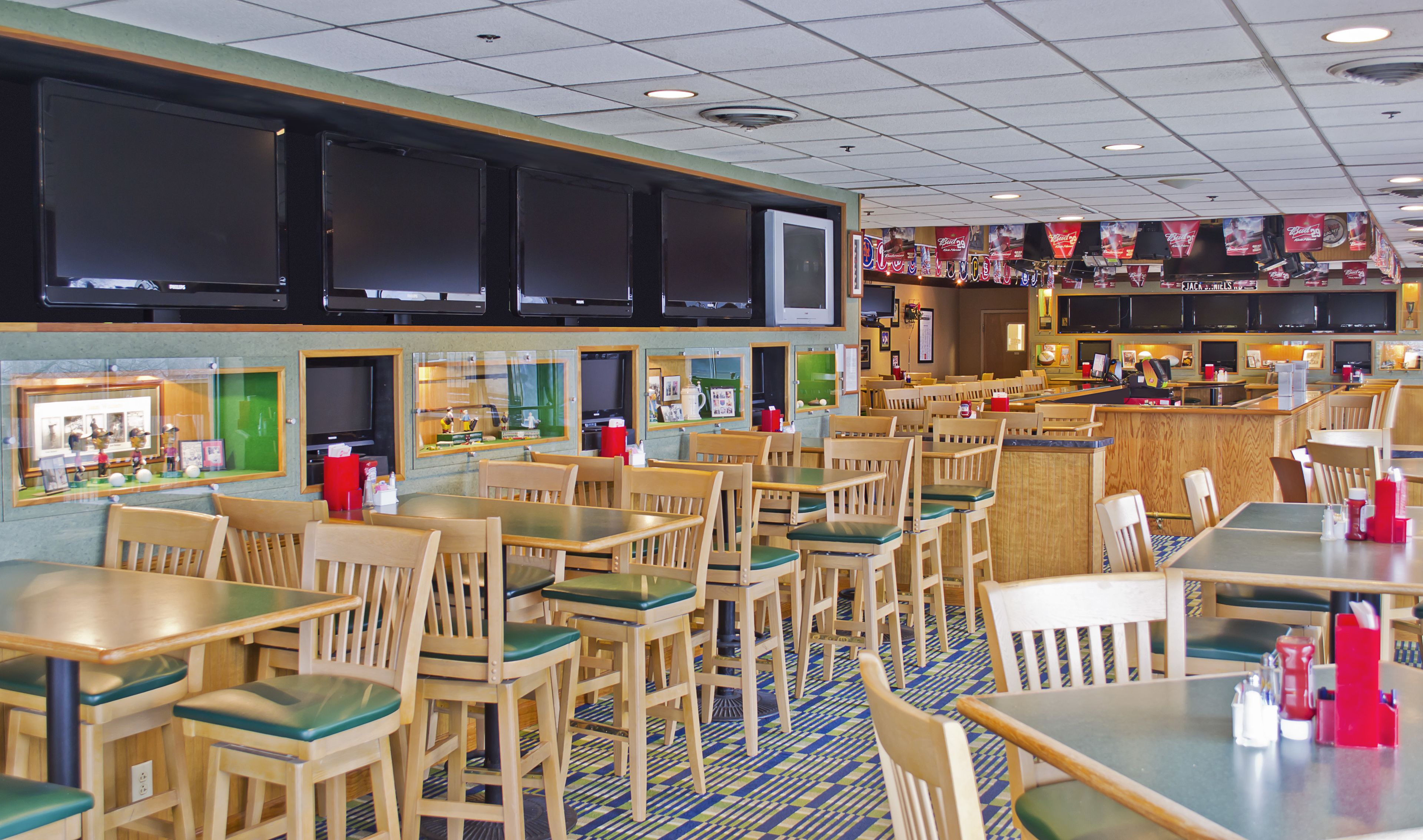 Ein Restaurant mit Holztischen und -stühlen, einer Theke und mehreren an der Wand befestigten Fernsehern.