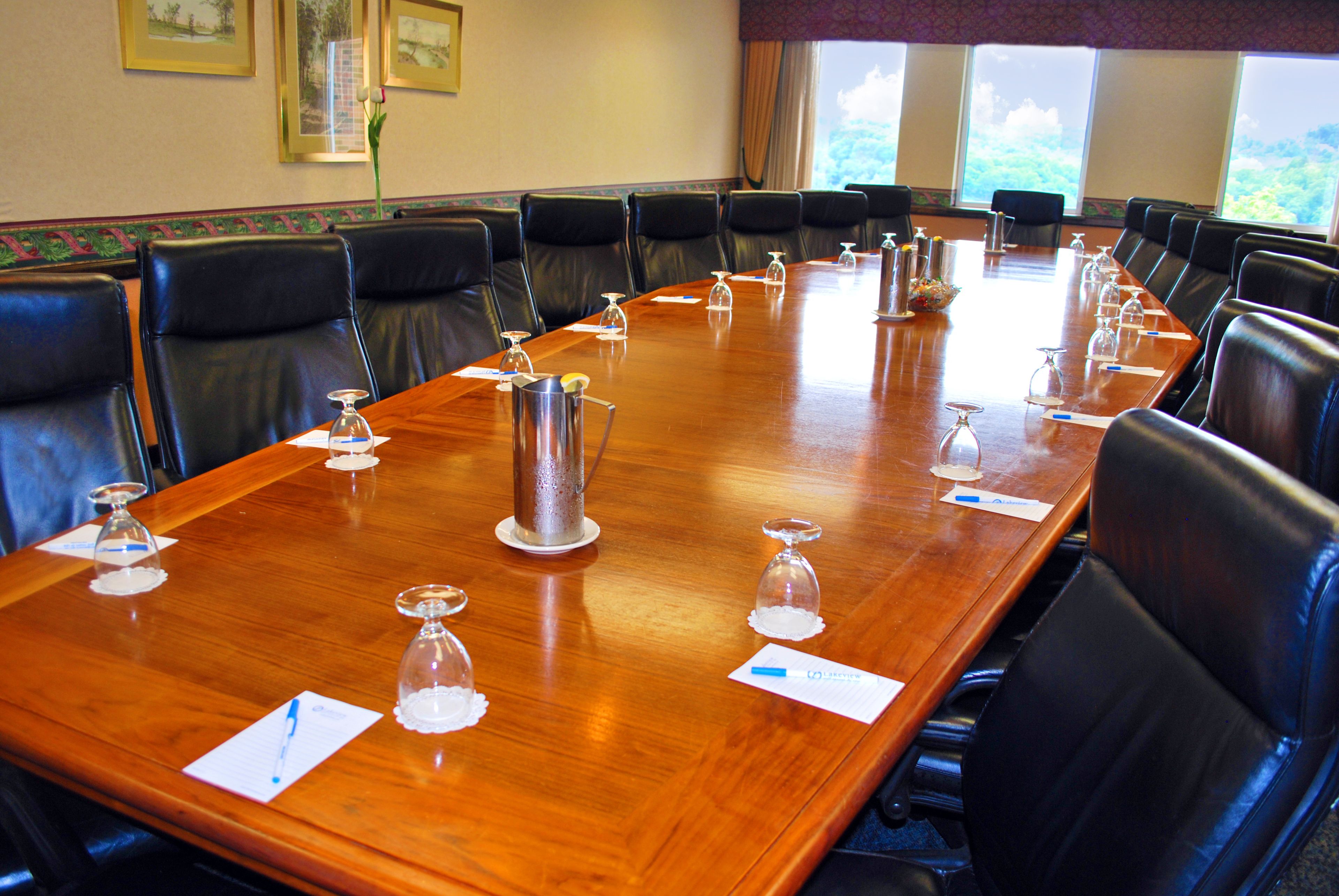 A conference room with a long wooden table, black leather chairs, and water glasses on the table.