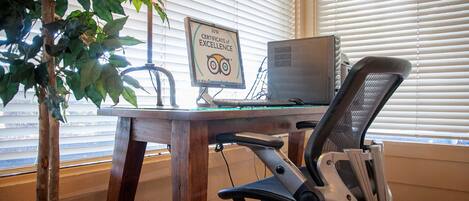 Un escritorio de madera con una computadora, una silla y un certificado de excelencia en la pared.
