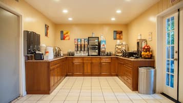 Una cocina con armarios de madera, un refrigerador, una cafetera y un cubo de basura.