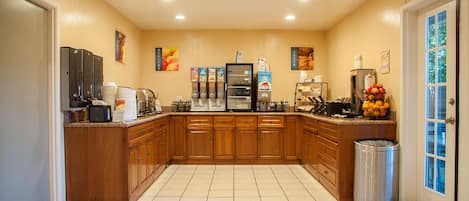 A kitchen with wooden cabinets, a refrigerator, a coffee machine, and a trash can.