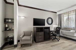 A modern hotel room with a desk, chair, television, and air conditioning unit.