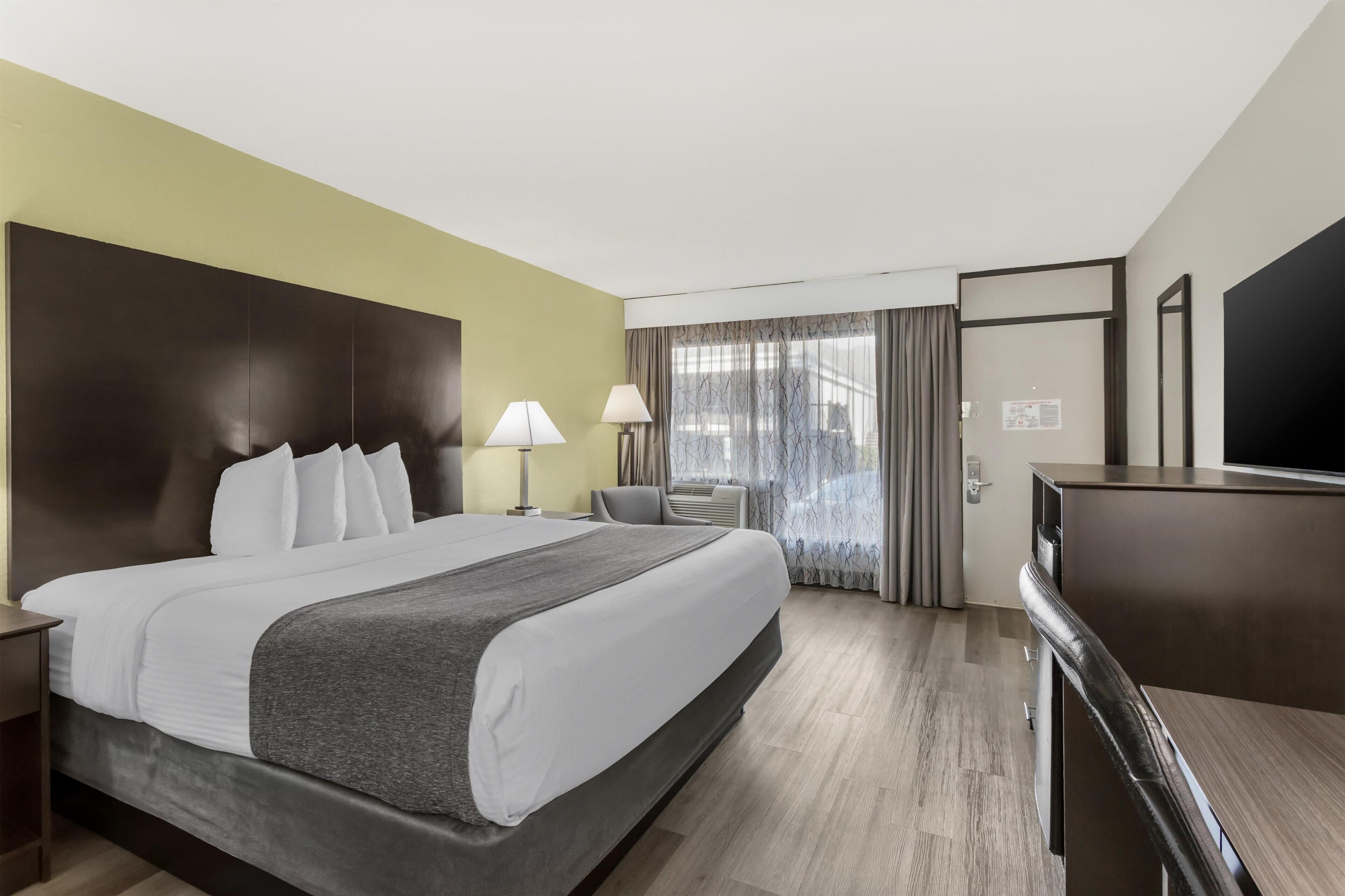 A hotel room with a large bed, bedside lamps, a desk, and a television.