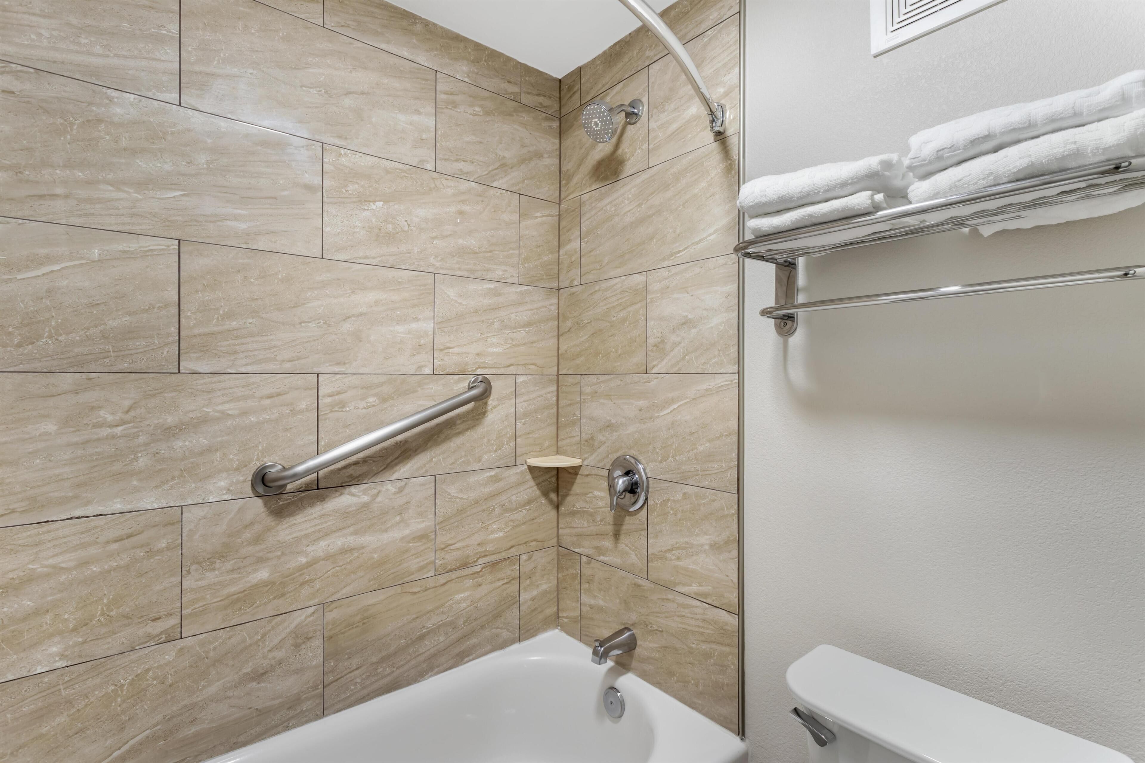 Un baño con bañera, ducha, barra de apoyo y toallero.