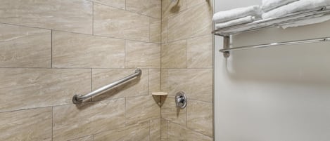 A bathroom with a bathtub, a shower, a handrail, and a towel rack.