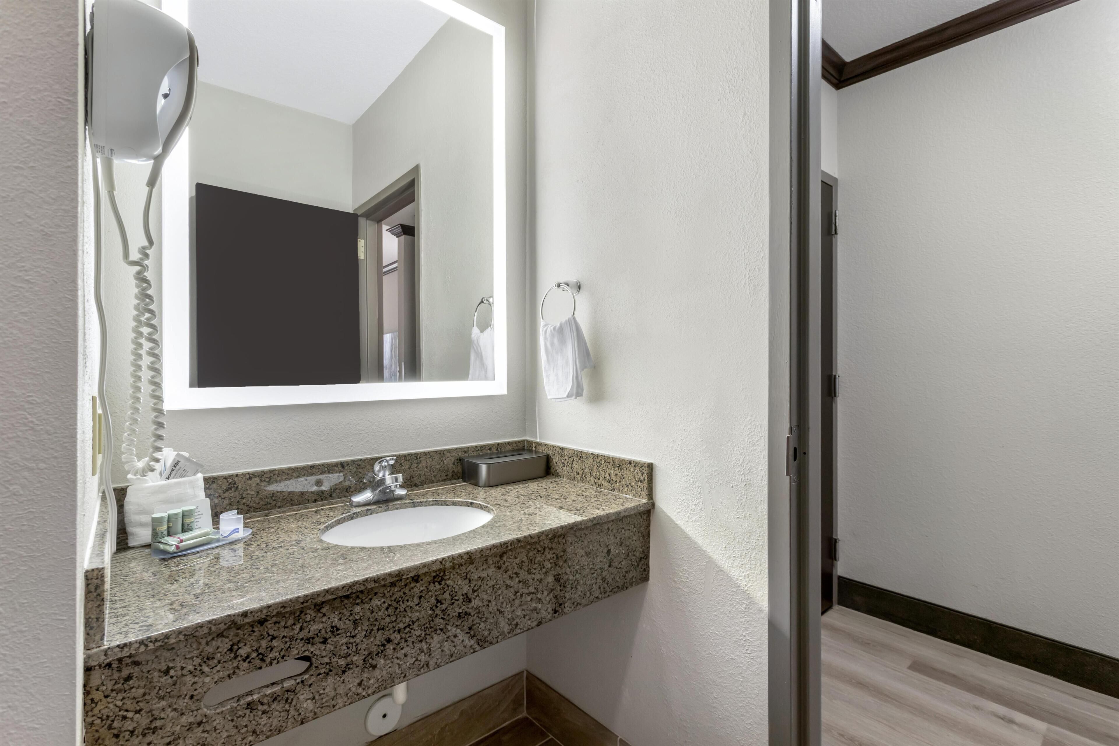 A bathroom with a granite countertop, a sink, a mirror, a hairdryer, and a towel rack.