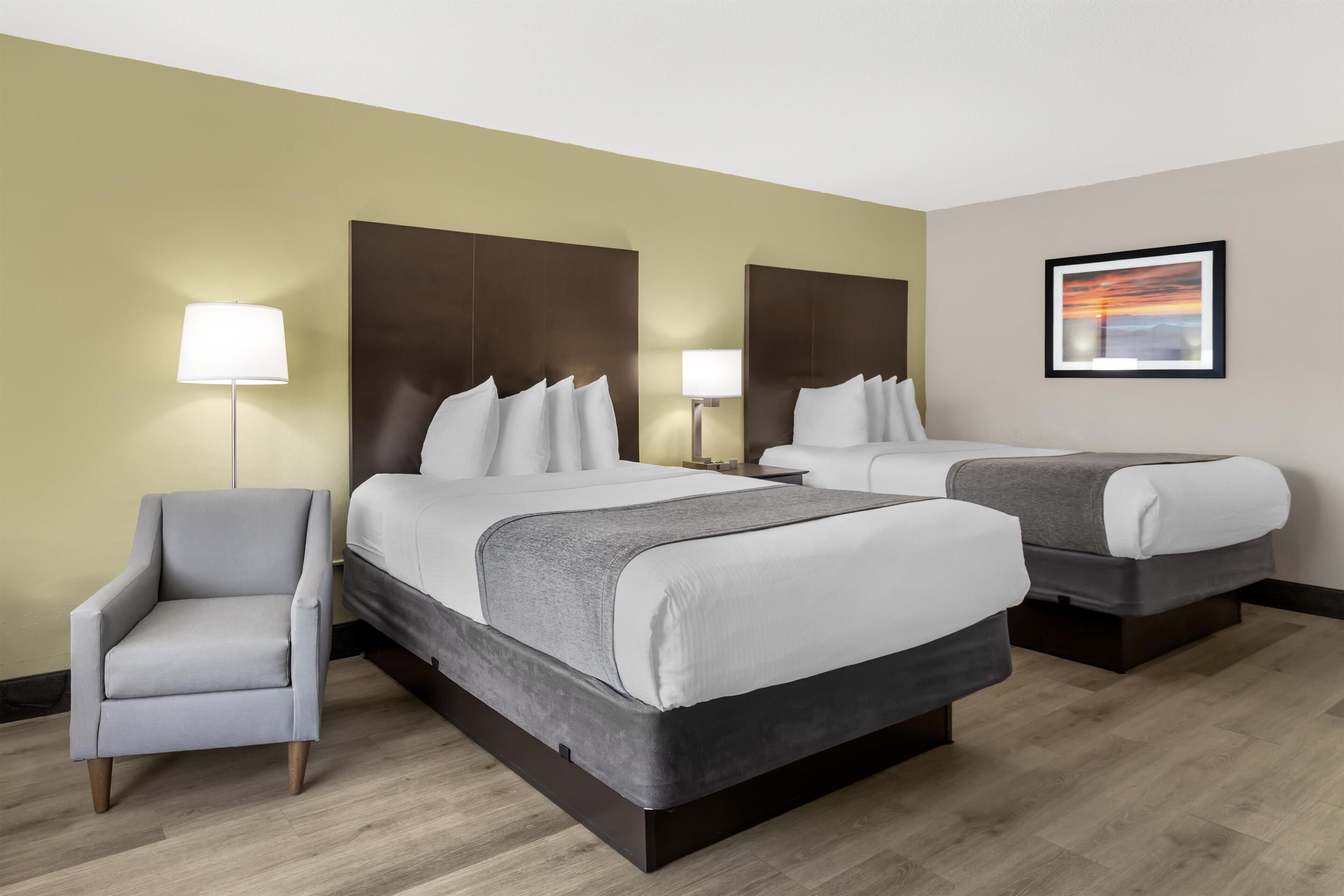 A hotel room with two beds, a chair, and a lamp.