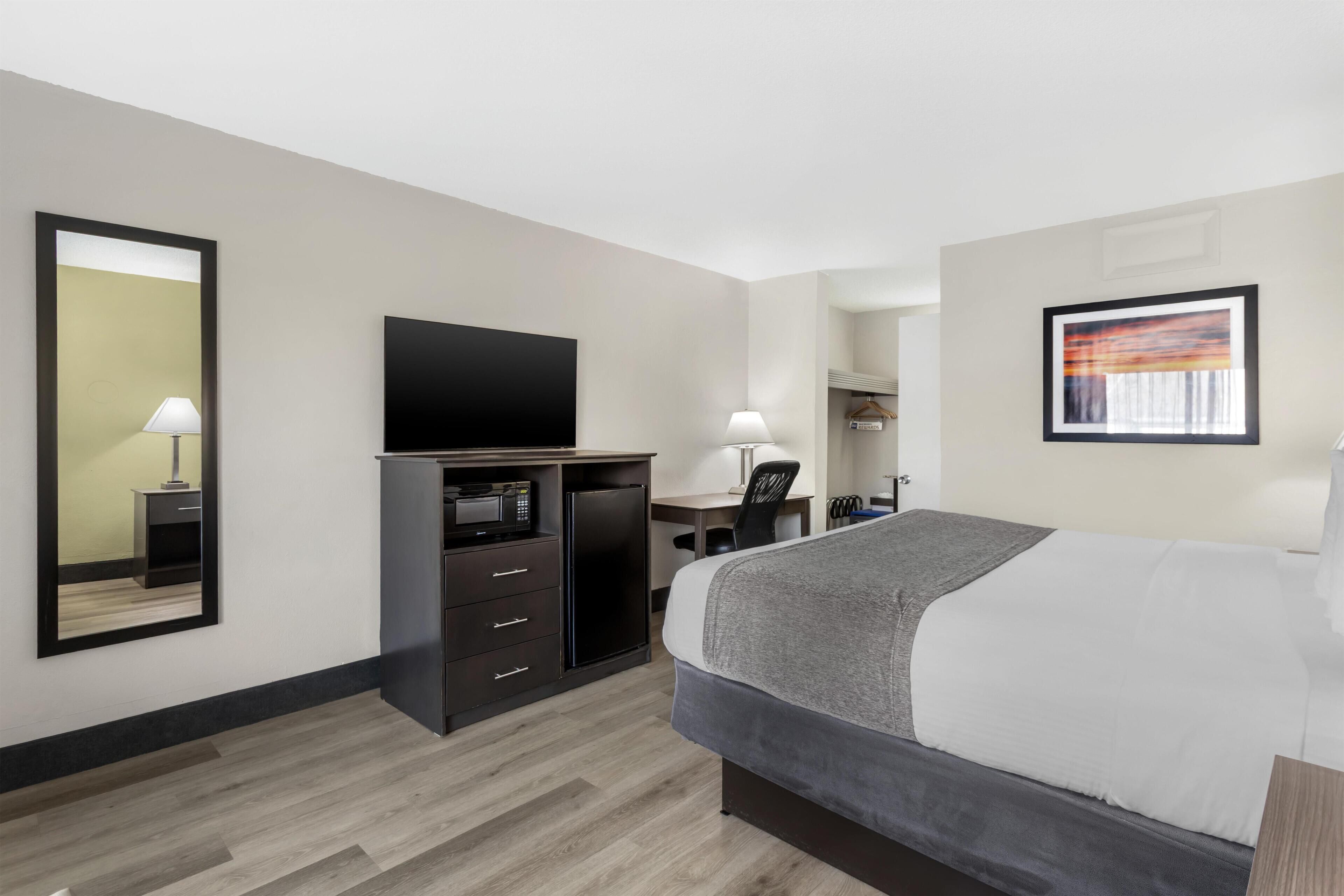 Quarto de hotel com uma cama, uma escrivaninha com computador, televisão e espelho.