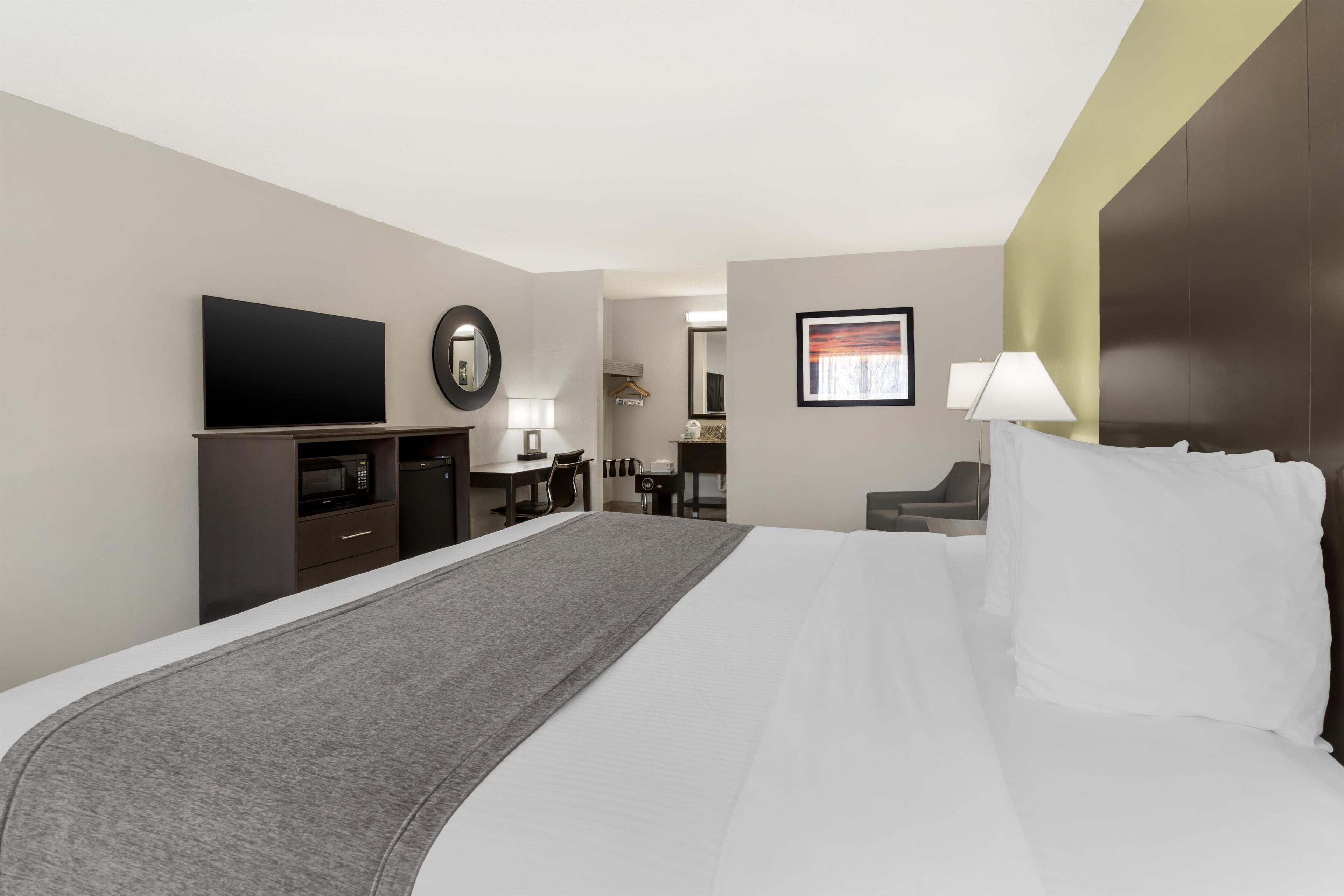 A hotel room with a large bed, a flat-screen TV, a desk with a chair, a lamp, and a framed picture on the wall.