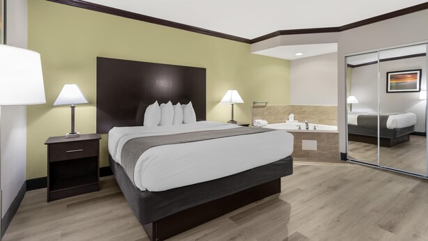A hotel room with a large bed, bedside lamps, a nightstand, a bathroom with a mirror, and a painting on the wall. - Best Western Asheville Blue Ridge Parkway (Asheville)