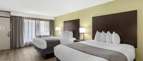 A hotel room with two beds, a large window with curtains, a wooden floor, and a dark headboard.